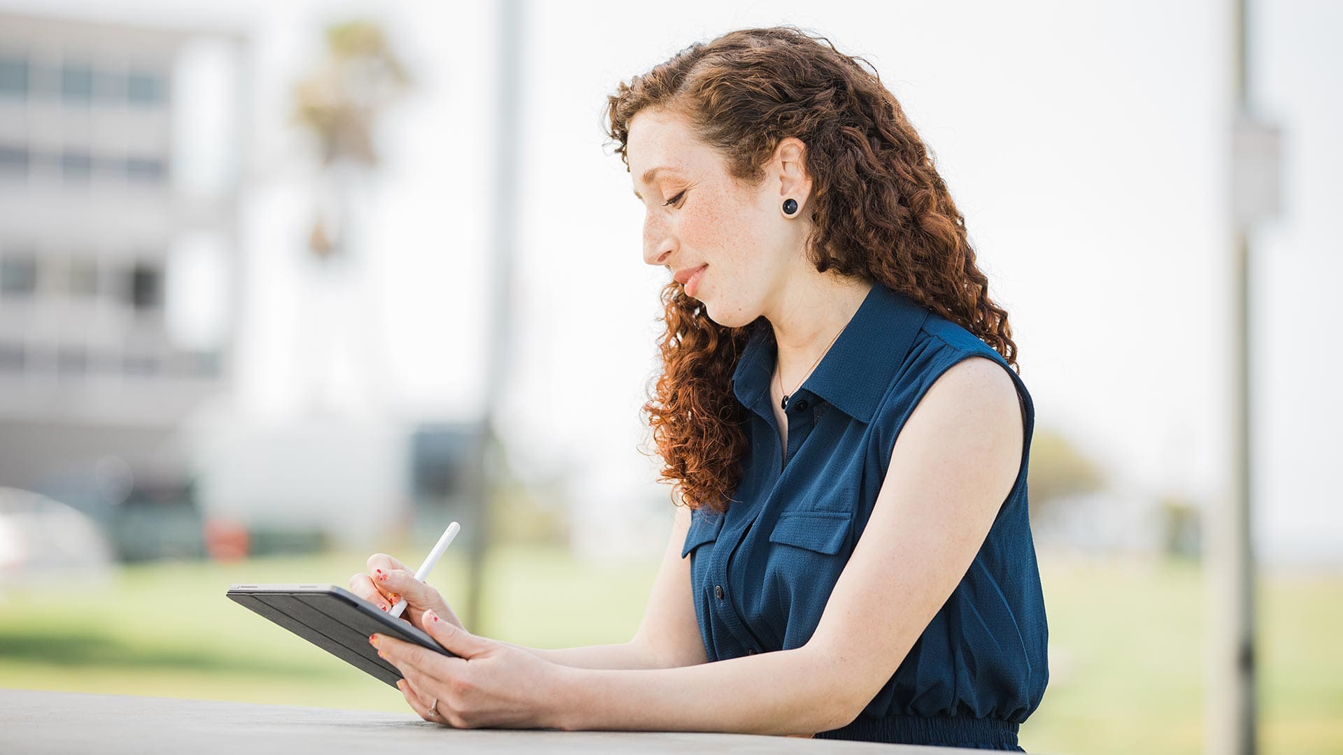 Mariel Embry, who earned her degree from SNHU in 2022, sitting at a table outside and usinsg a stylus to write  on a tablet computer.