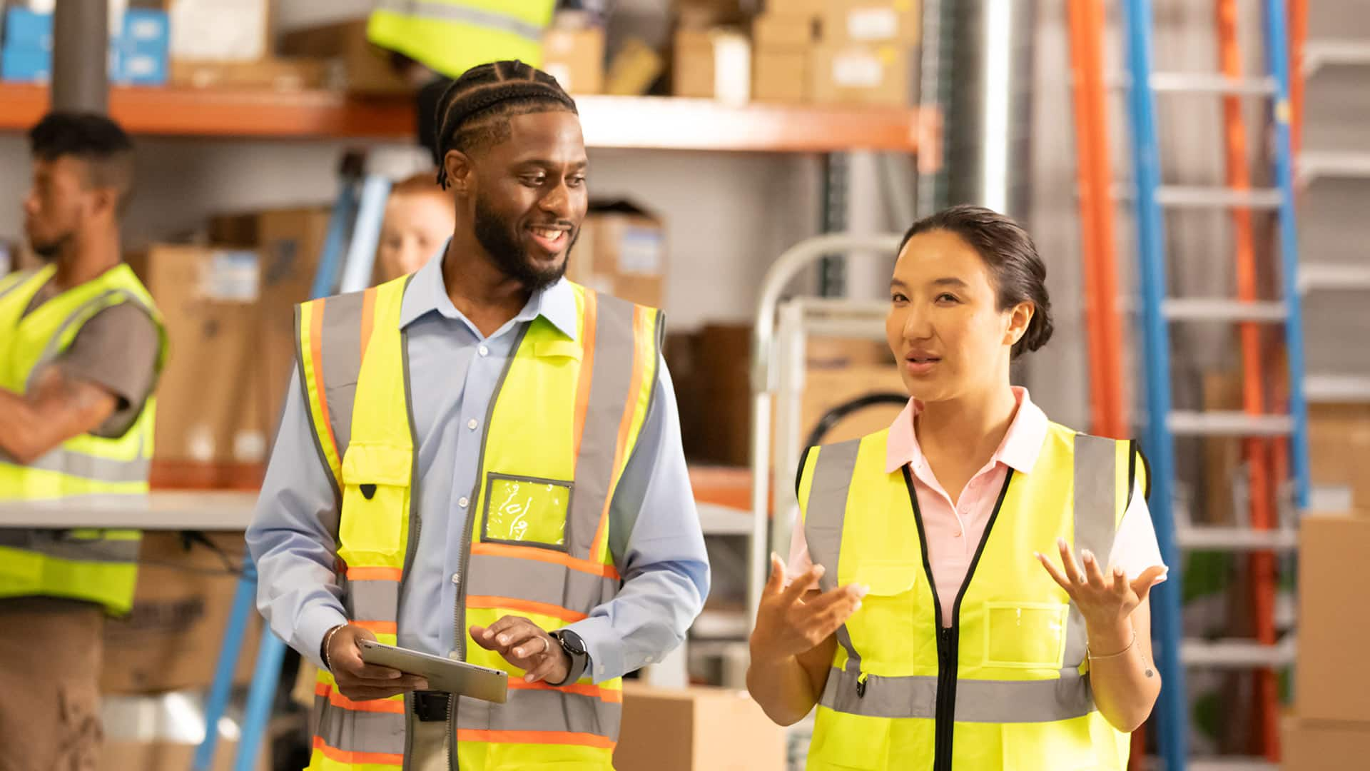 Matthrew Seawright, who earned a degree from SNHU in 2019, wearing a bright yellow safety vest and holding a tablet computer speaking to a woman inside a warehouse.