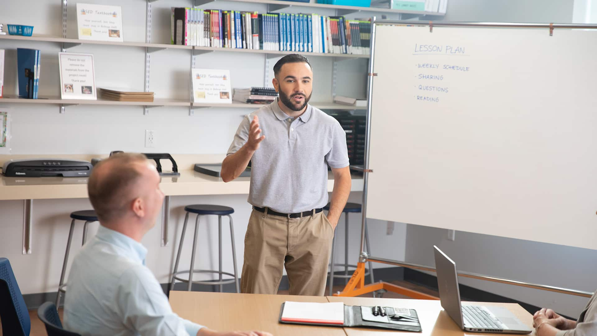 Stephen Goulakos, a 2022 psychology degree online graduate, standing in a meeting room speaking to a group of other business professionals with a white board in the background