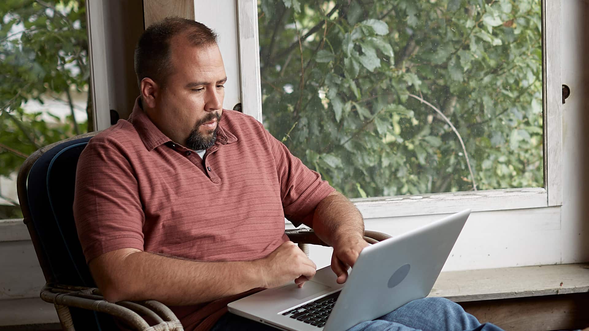 Raymond Gammon, who earned his MS in Data Analytics in 2020, sitting in a wicker chair on his porch with his feet up and his laptop on his legs in front of him.