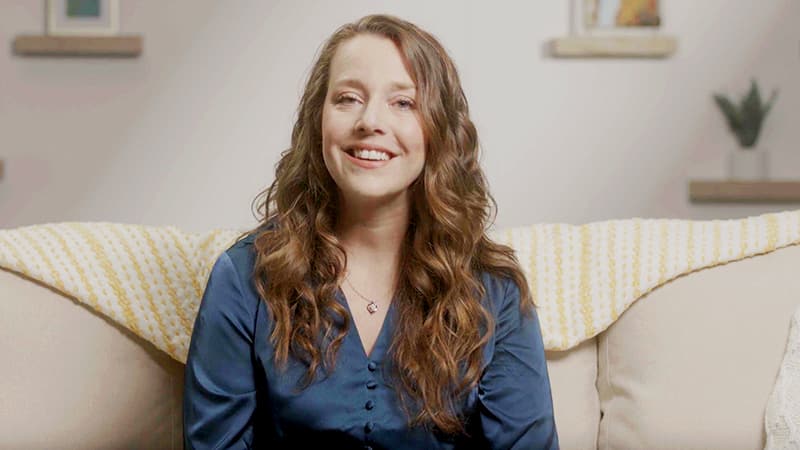 Julianne Hunter, who earned a degree in higher education administration in 2023, sitting on a white couch wearing a dark blue blouse and smiling.