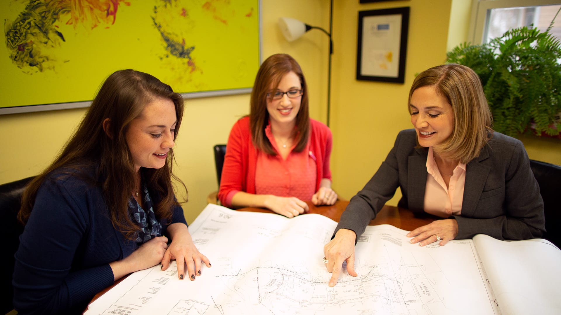 "Marti Ilg, who earned her degree from SNHU in 2014, sitting at a table with two other women pointing out a detail on  a large property map covering the table."