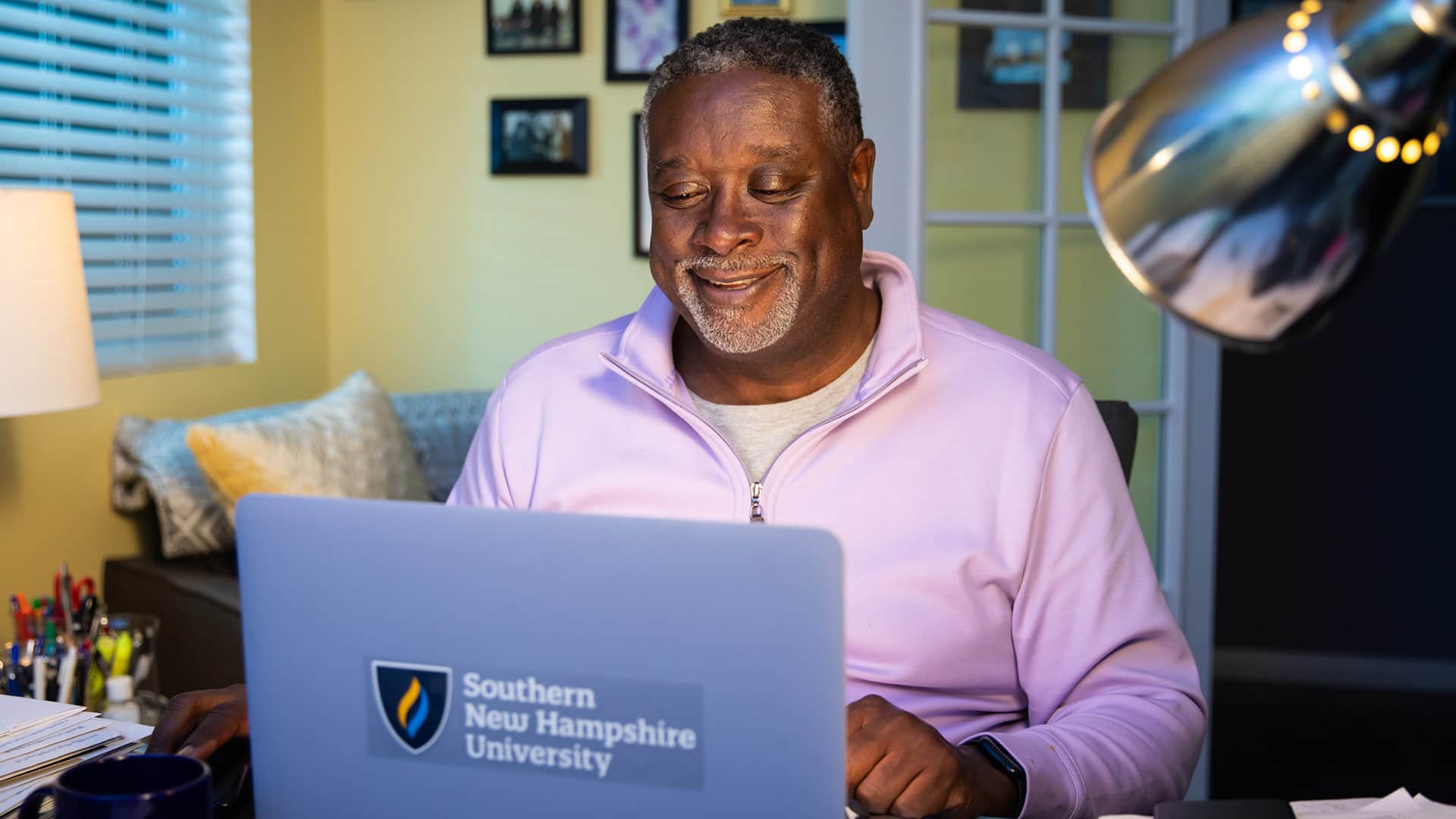Corey Dantzler, who earned his degree from SNHU in 2023, in his home office working on his laptop with a Southern New Hampshire University sticker on the front.