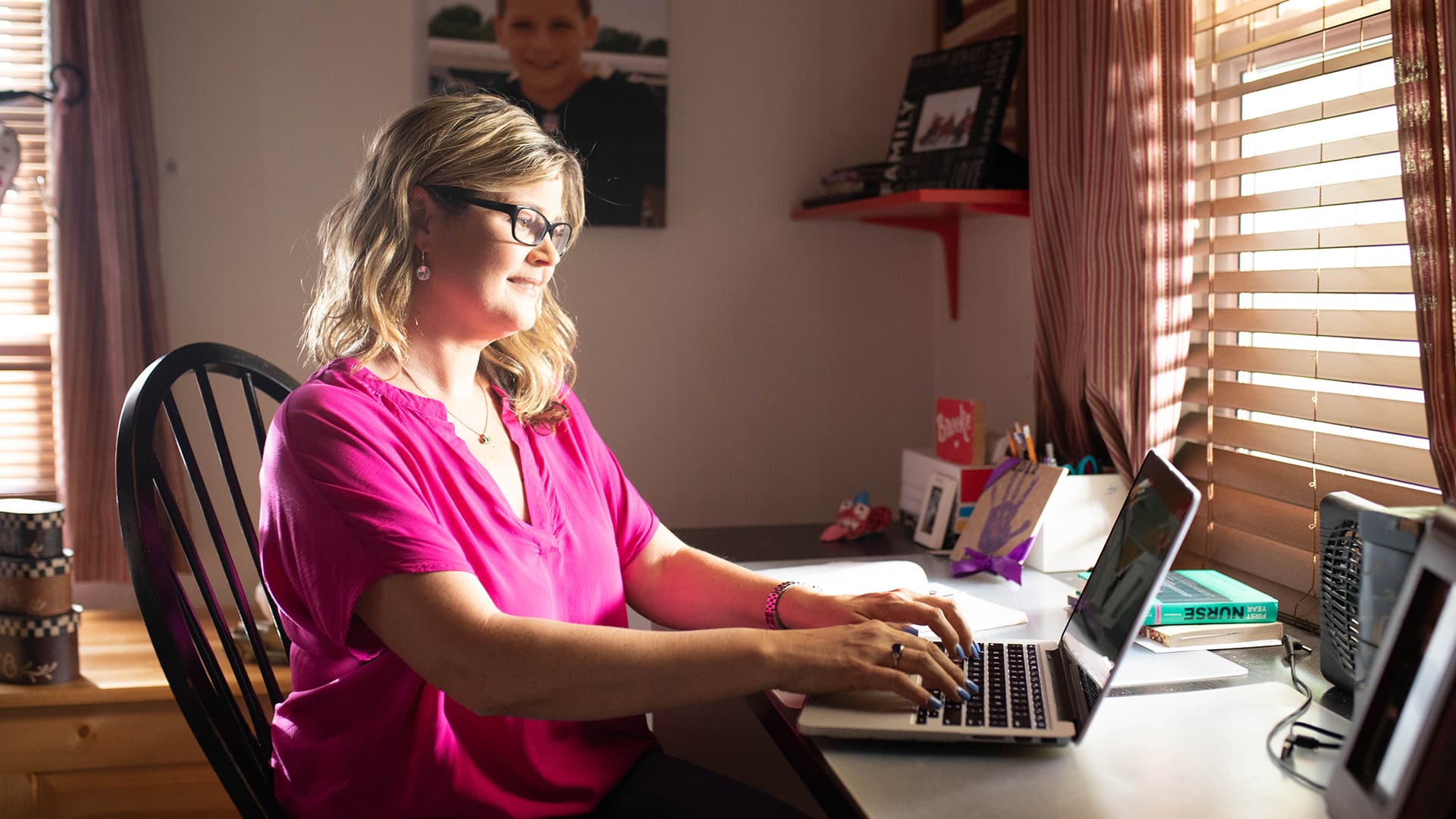 Kristina Libby, who earned her nursing degree from SNHU in 2017, in her home office wearing a pink blouse and working on her laptop. 