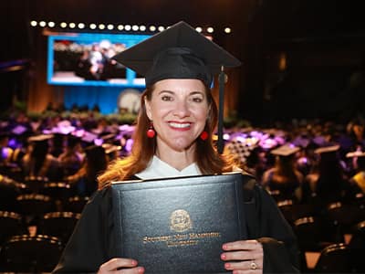 Donna Parisi, who earned her online master's in creative writing from SNHU in 2024, wearing her cap and gown and holding her diploma.