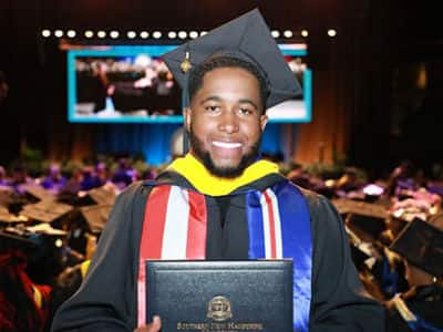 Pedro Borges, who earned his bachelor's in business administration from SNHU, wearing his graduation cap and gown and holding his diploma.