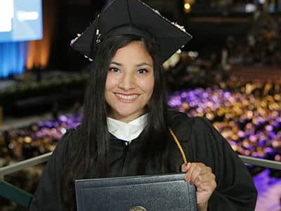 Savannah Martinez, who earned her bachelor's degree in psychology from SNHU, wearing her cap and gown and holding her diploma.