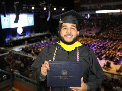 Remus Figueroa Orozco '23, who earned his bachelor's in cybersecurity from SNHU, wearing his cap and gown and holding his diploma.