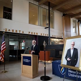 SNHU President Paul LeBlanc to the left of his portrait, sharing remarks inside the Paul J. LeBlanc Hall on campus.