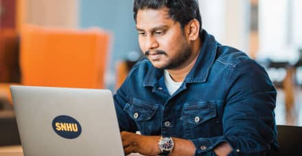 A young man with dark hair works at a laptop.