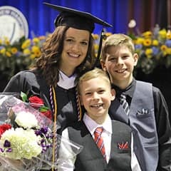 Tarah Theis dressed in a graduation cap and gown, to the left of her two sons, after earning a bachelor's in communication at SNHU in 2022