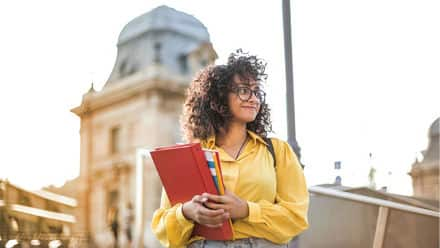 A person in a yellow shirt holding binders and considering affordable online colleges.