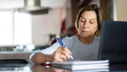 A person researching how to go back to college on a laptop and taking notes with a pen