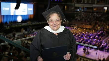 Mary Beth Dayley '24G, an SNHU Masters in English and Creative Writing graduate, in a cap and gown holding her diploma.