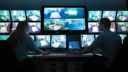 Two homeland security professionals monitoring a series of security camera feeds