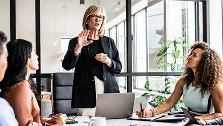 A director of operations standing at the end of a table running a team meeting