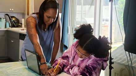 Latisha Aguilar '21, an SNHU graduate with a bachelor's in psychology, helping her daughter with homework at the kitchen table 