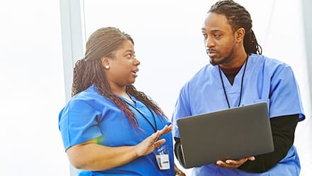 Two nurses working on a laptop while discussing how long it takes to become a nurse