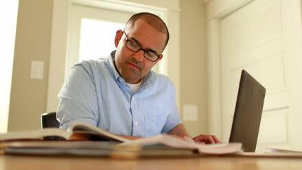 A man with a light blue shirt and glasses looking up how to stay motivated in college on a laptop.