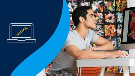 A graphic designer working at his desk next to a blue background with a computer and paintbrush on it.