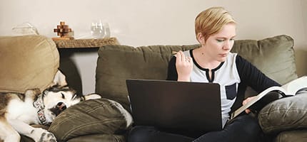 Jolene Stetz studying a textbook with a laptop in front of her and dog asleep beside her.