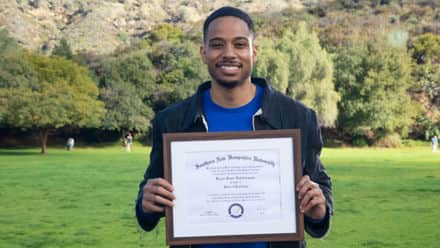 Keyon Tuiteleleapaga holding his SNHU diploma after earning a master's degree in psychology in 2024