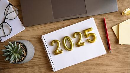 2025 represented in gold lettering on a notebook with a pen, plant and laptop beside it