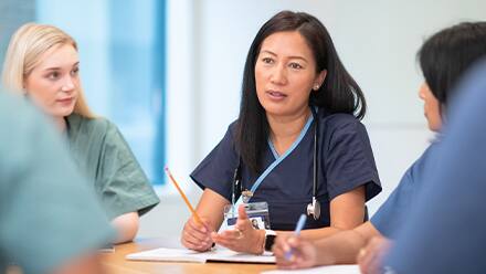 A nurse leader with a stethoscope, leading a meeting with a group of other nurses