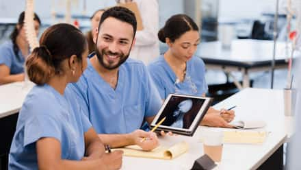 Three nurses in blue scrubs, working together in a professional development seminar