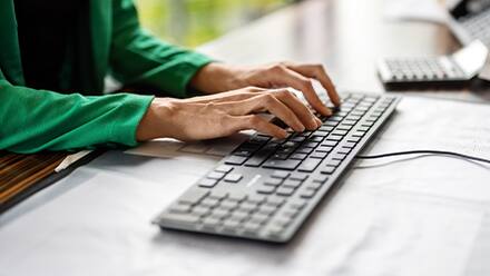 A person wearing a green top typing on a keyboard working as a technical writer.