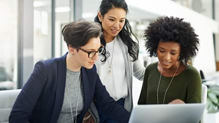 Three business professionals reviewing a presentation on a laptop.