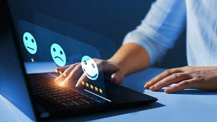 A customer experience professional typing on a laptop with three emoji icons representing levels of satisfaction