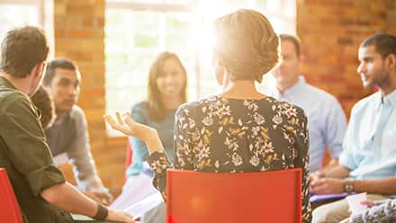 Eight professionals sitting in a circle while one describes what organizational leadership is.