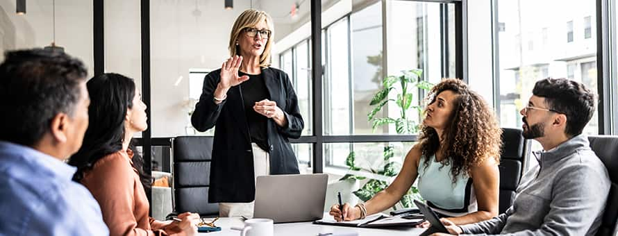 A director of operations standing at the end of a table running a team meeting