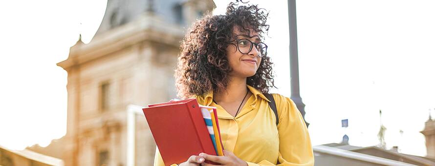 A person in a yellow shirt holding binders and considering affordable online colleges.