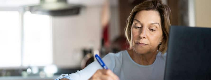 A person researching how to go back to college on a laptop and taking notes with a pen