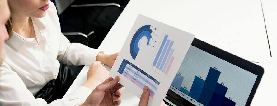 Two actuary's sitting together looking over charts and graphs on a piece of paper and a laptop.