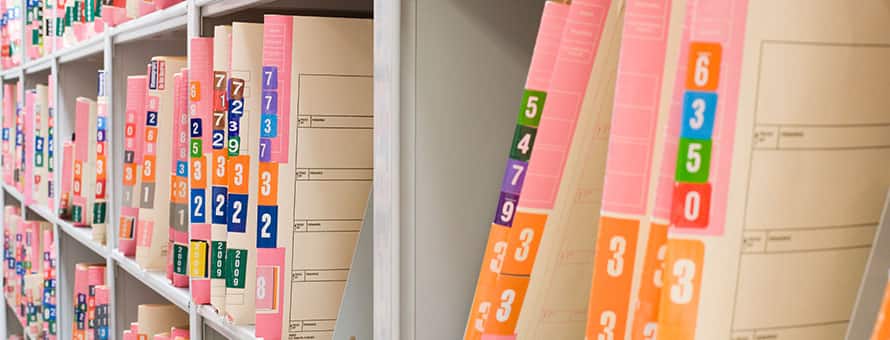 A shelf filled with medical files stored in manilla folders.