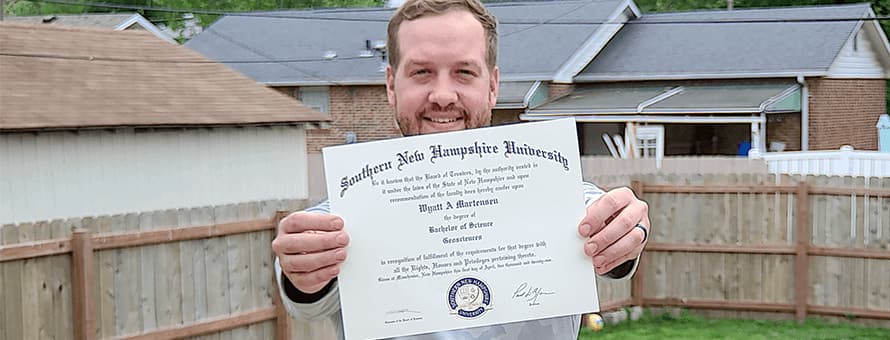 Wyatt Martensen standing outside proudly showing off his SNHU diploma.