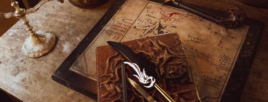 A quill and notebook sitting atop a map on weathered desk, surrounded by antique looking objects.