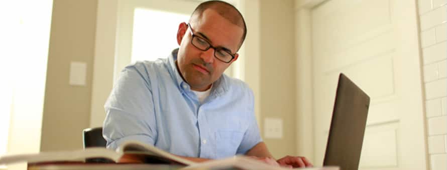 A man with a light blue shirt and glasses looking up how to stay motivated in college on a laptop.