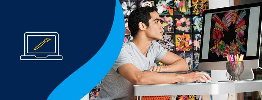 A graphic designer working at his desk next to a blue background with a computer and paintbrush on it.