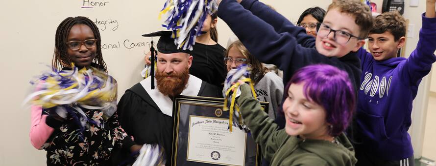 Ryan Manning in his cap and gown holding his diploma surrounded by his students