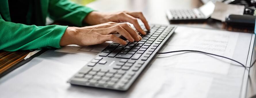 A person wearing a green top typing on a keyboard working as a technical writer.