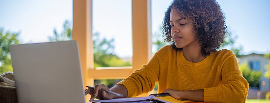 A student in a yellow sweater sitting at a desk working on her minor on her laptop