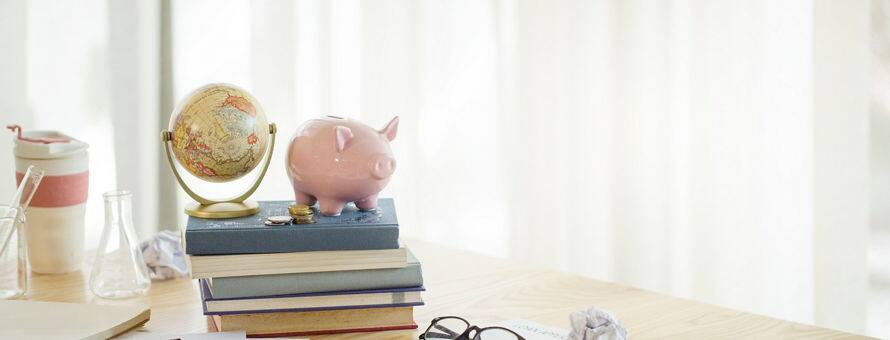 A desk with papers, a phone, and a stack of books with a piggy bank and globe on top