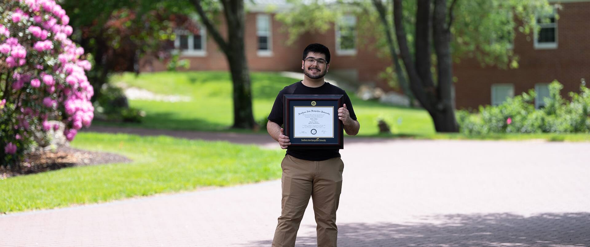 Sultan Ahktar, who earned his degree from SNHU in 2019, standing on a quiet street holding his framed diploma.