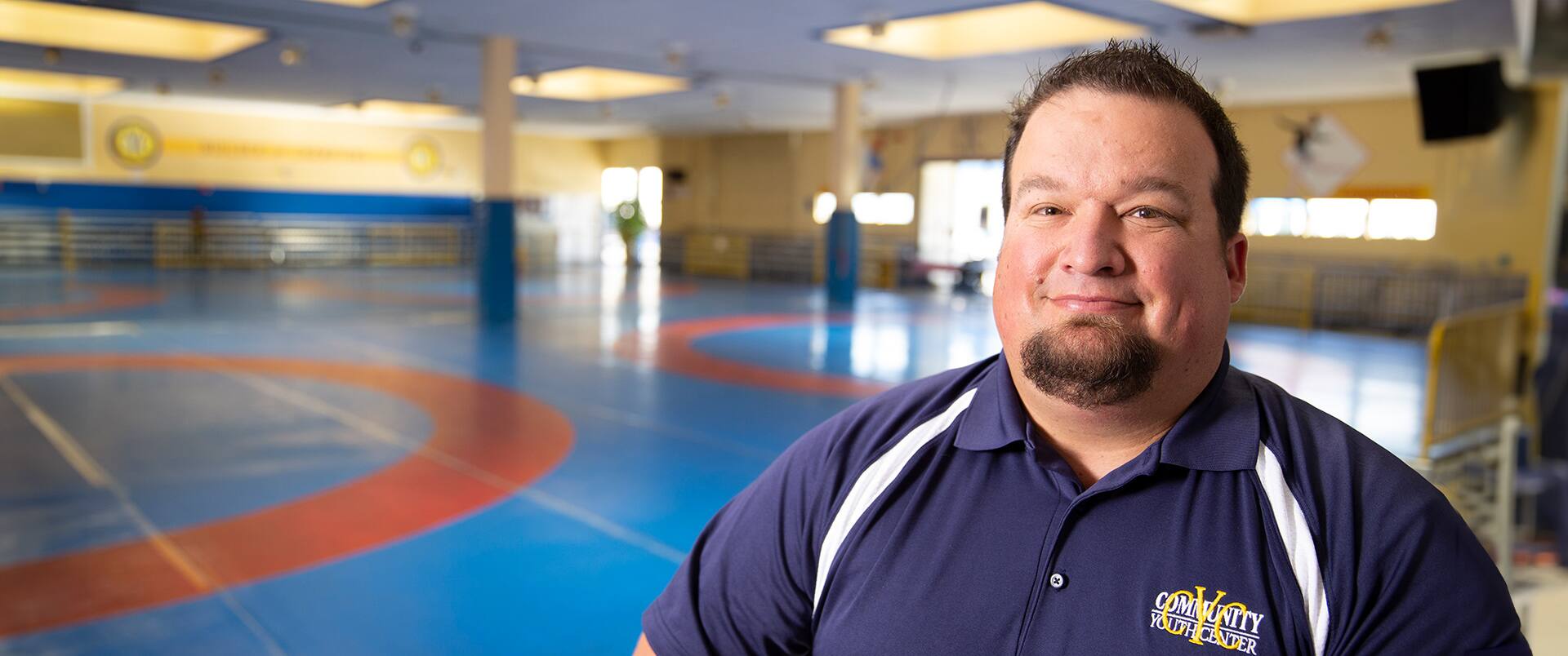 Matt Martin, a 2015 sport management online degree graduate, sitting inside a wrestling gymnasium.