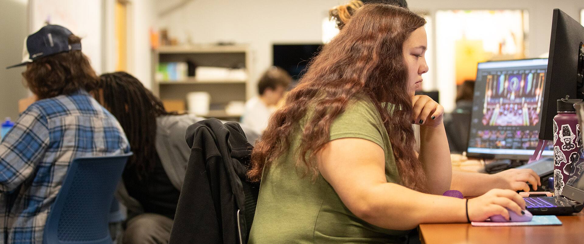 A couple of students and an instructor sitting at computers in a computer lab.