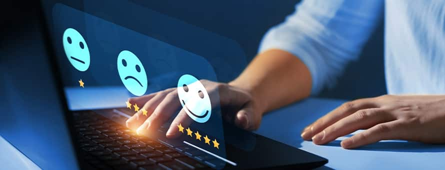 A customer experience professional typing on a laptop with three emoji icons representing levels of satisfaction